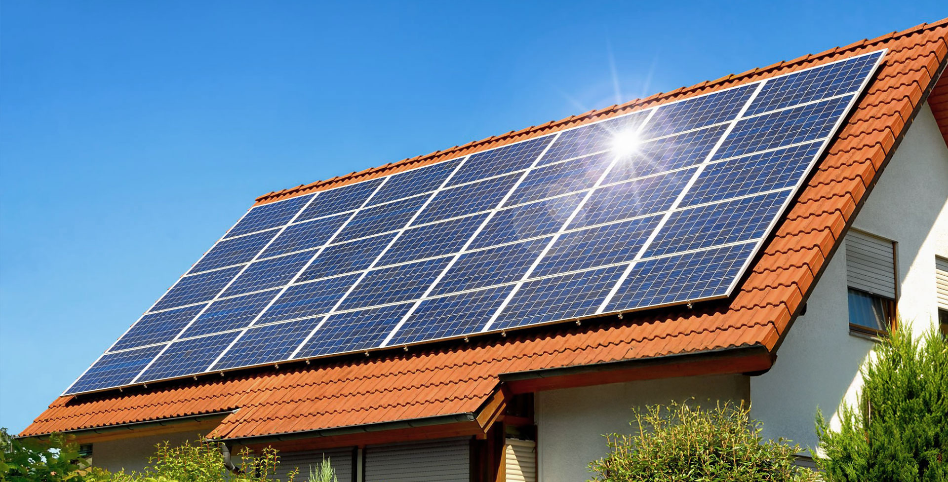 Solar panels on a terracotta tiled residential roof under a bright blue sky